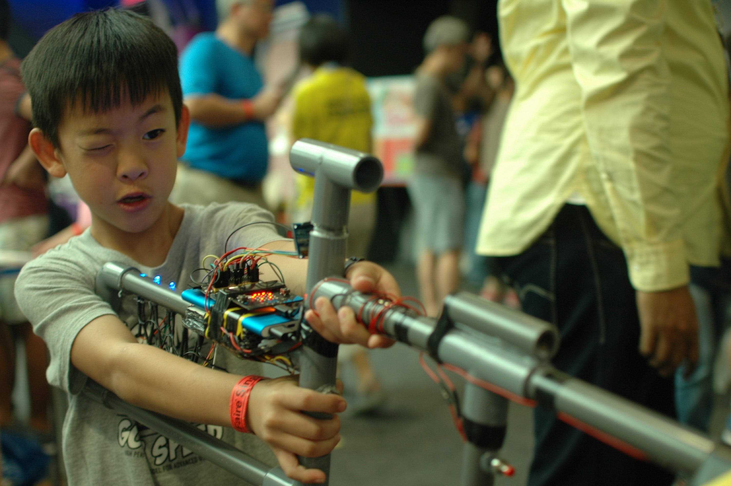 Child operates the improvised electronic gun, with exposed wires and red tape around its frame.