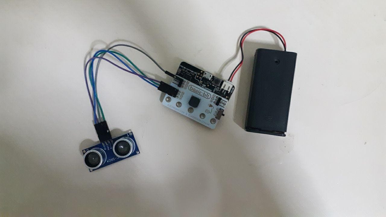 Microcontroller wired to an ultrasonic distance sensor and battery pack on a worktable.