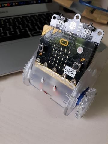 Transparent Ring:bit robot car with an exposed circuit board and LED matrix beside a laptop.