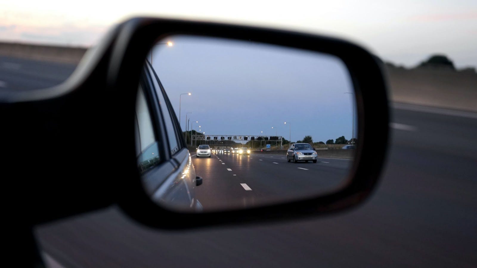 Traffic reflected in a car’s side-view mirror on a highway at dusk