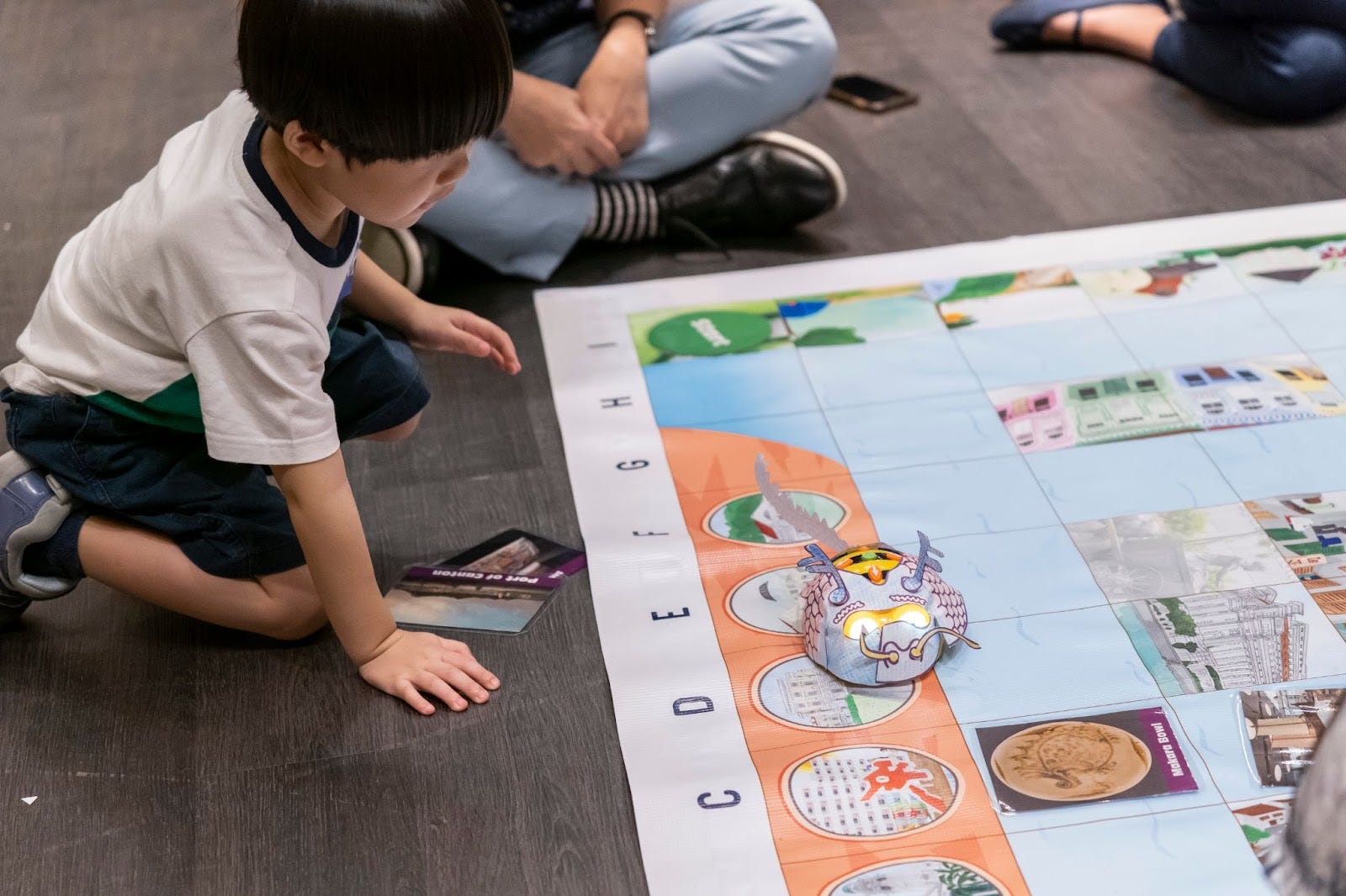 Child watches a Bee-Bot travel across a large illustrated grid mat during the workshop.