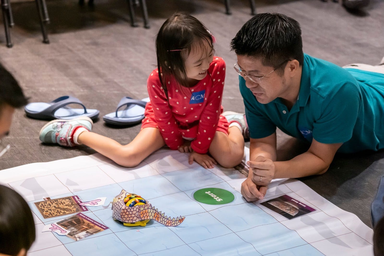 Child and adult sit together beside a Bee-Bot on an activity mat marked ‘Start.’